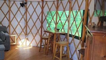 A tent with a wooden lattice structure, a dining table with chairs, a sofa, a cabinet, and a patterned rug.