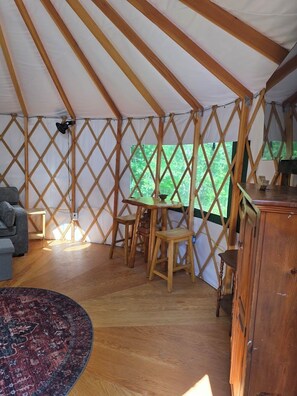 A tent with a wooden lattice structure, a dining table with chairs, a sofa, a cabinet, and a patterned rug. - Old Apple Orchard Yurt 2 (Buckfield)