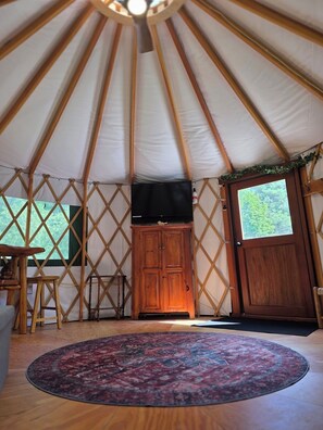 L’intérieur d’une yourte, avec une porte en bois, un meuble, un téléviseur et un tapis à motifs.
