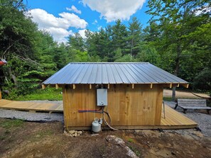 Eine kleine Holzhütte mit einem Metall-Dach, einem Warmwasserbereiter und einer Holzterrasse.