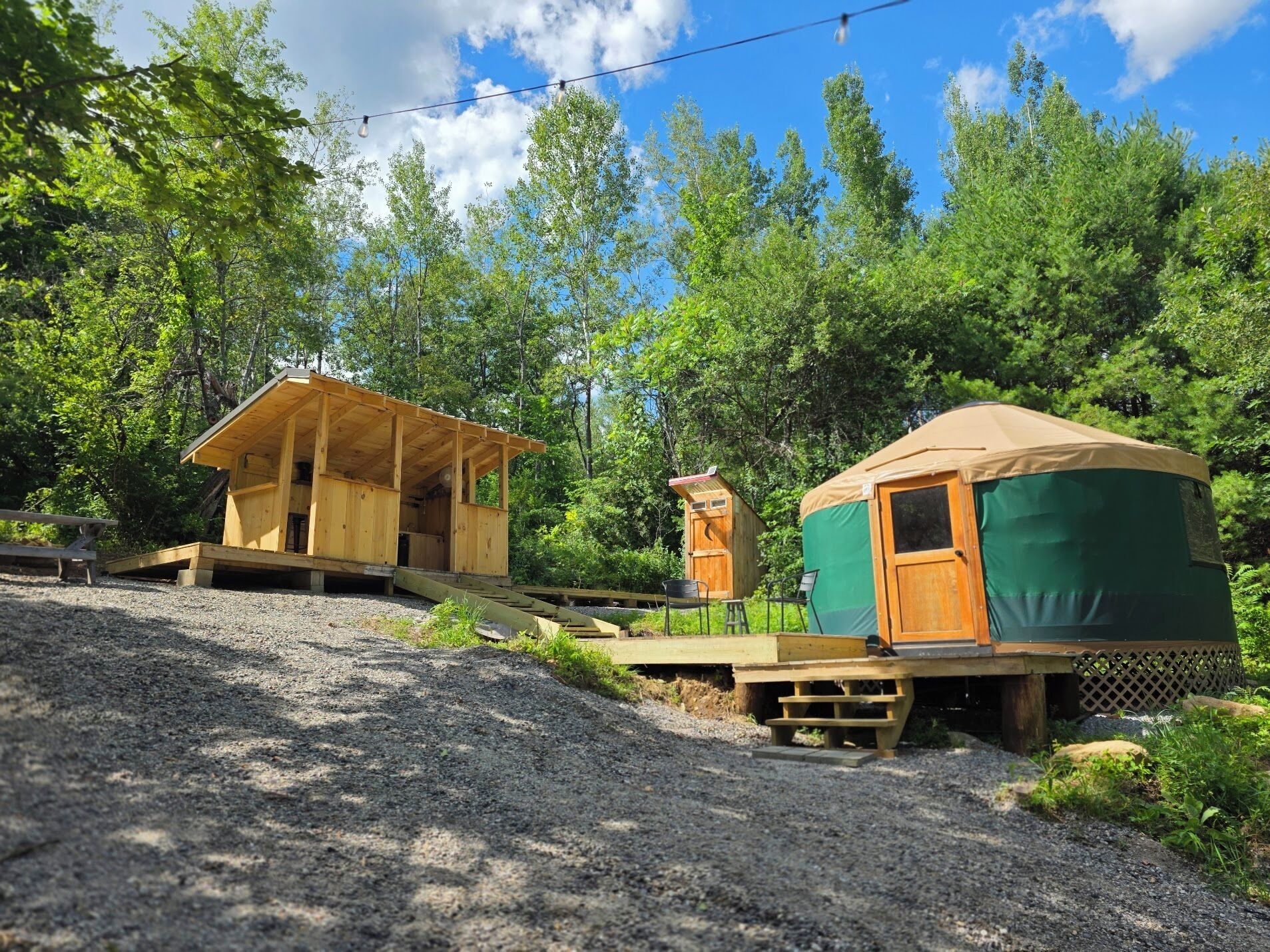 A rustic wooden cabin with a covered porch, a small wooden structure, and a green tent-like structure.