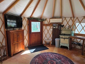 A yurt interior with a television, wooden cabinets, a stove, and a patterned rug. - Old Apple Orchard Yurt 2 (Buckfield)