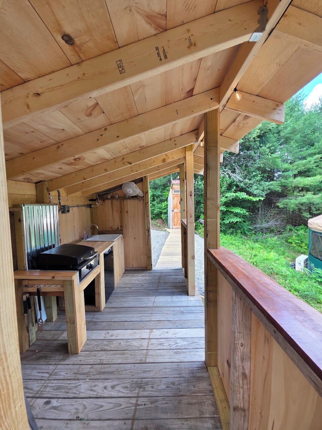A wooden deck with a grill and a table, surrounded by natural greenery.