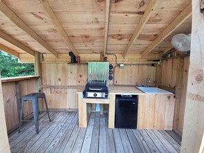 Eine hölzerne Außenküche mit Grill, Spüle und Geschirrspüler.