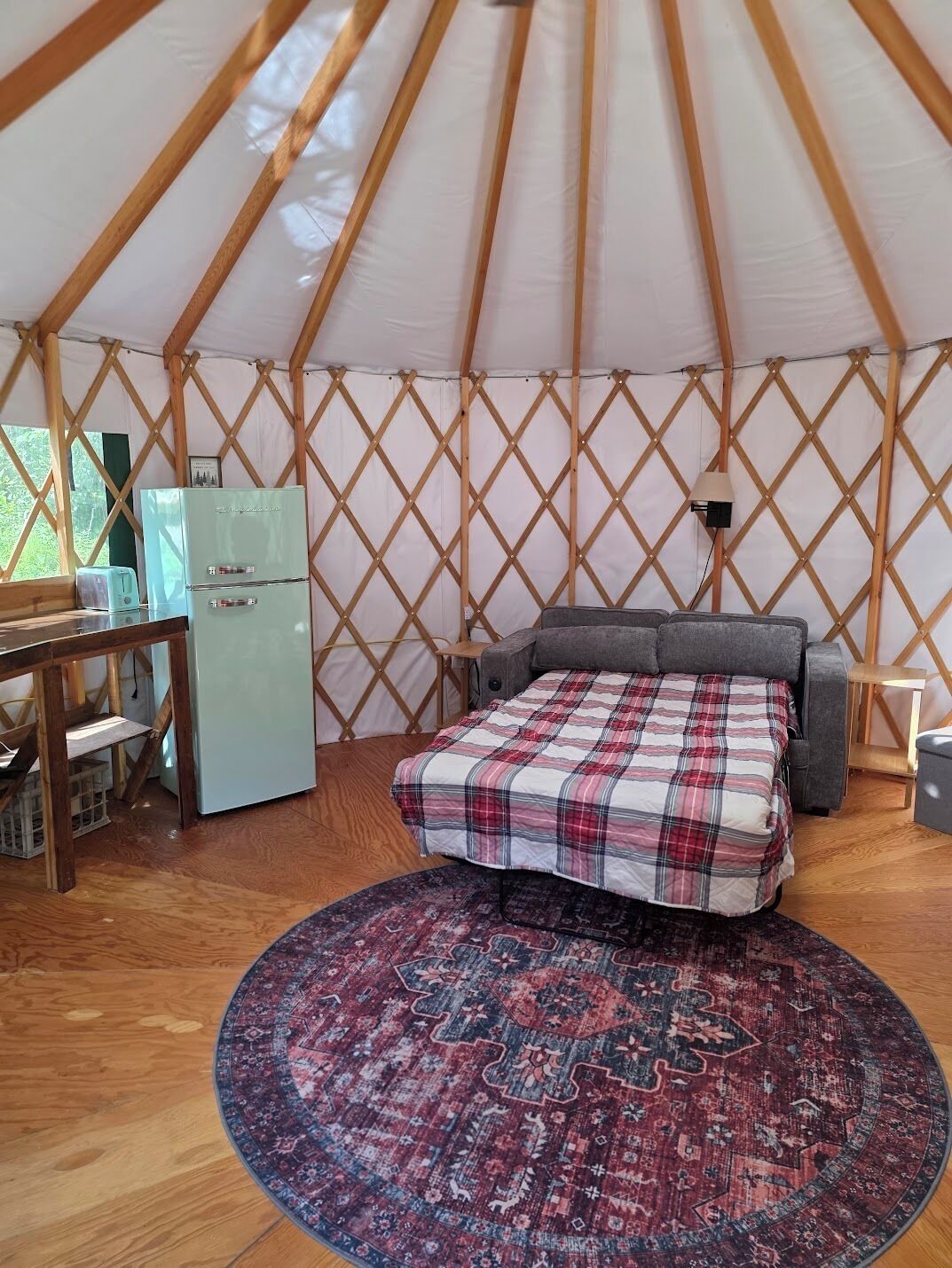 A yurt interior with a bed, a small kitchenette, and a round rug.
