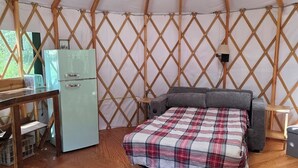 L’intérieur d’une yourte, avec un lit, une petite kitchenette et un tapis rond.