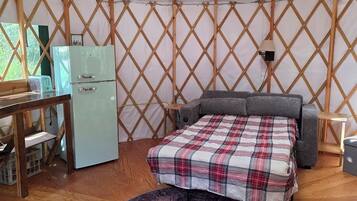 A yurt interior with a bed, a small kitchenette, and a round rug.