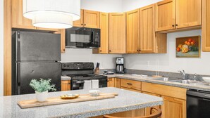 Una cucina con mobili in legno, un frigorifero nero, un forno a microonde, un fornello e una macchina per il caffè.