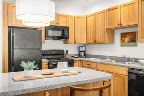 A kitchen with wooden cabinets, a black refrigerator, a microwave, a stove, and a coffee maker. - Lower Columbia Landing | 2BR Near Glacier (Columbia Falls)