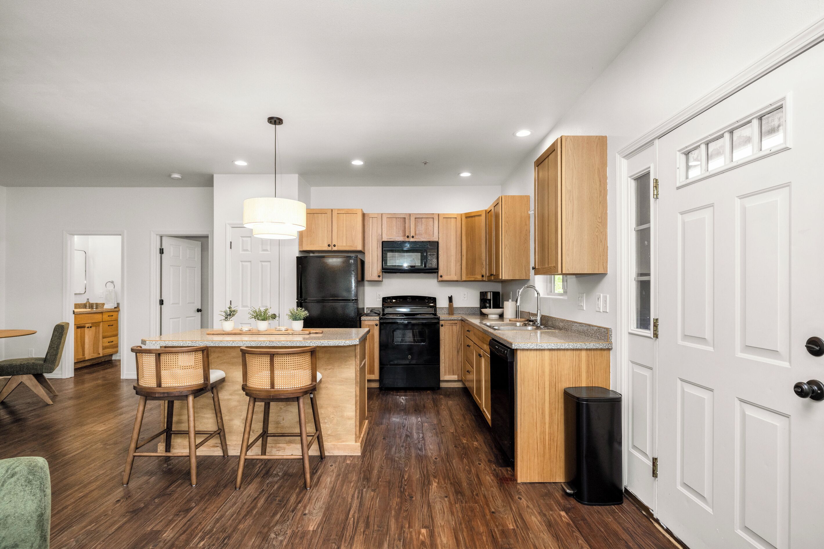 A modern kitchen with wooden cabinets, a black refrigerator, a microwave, and a central island with bar stools.