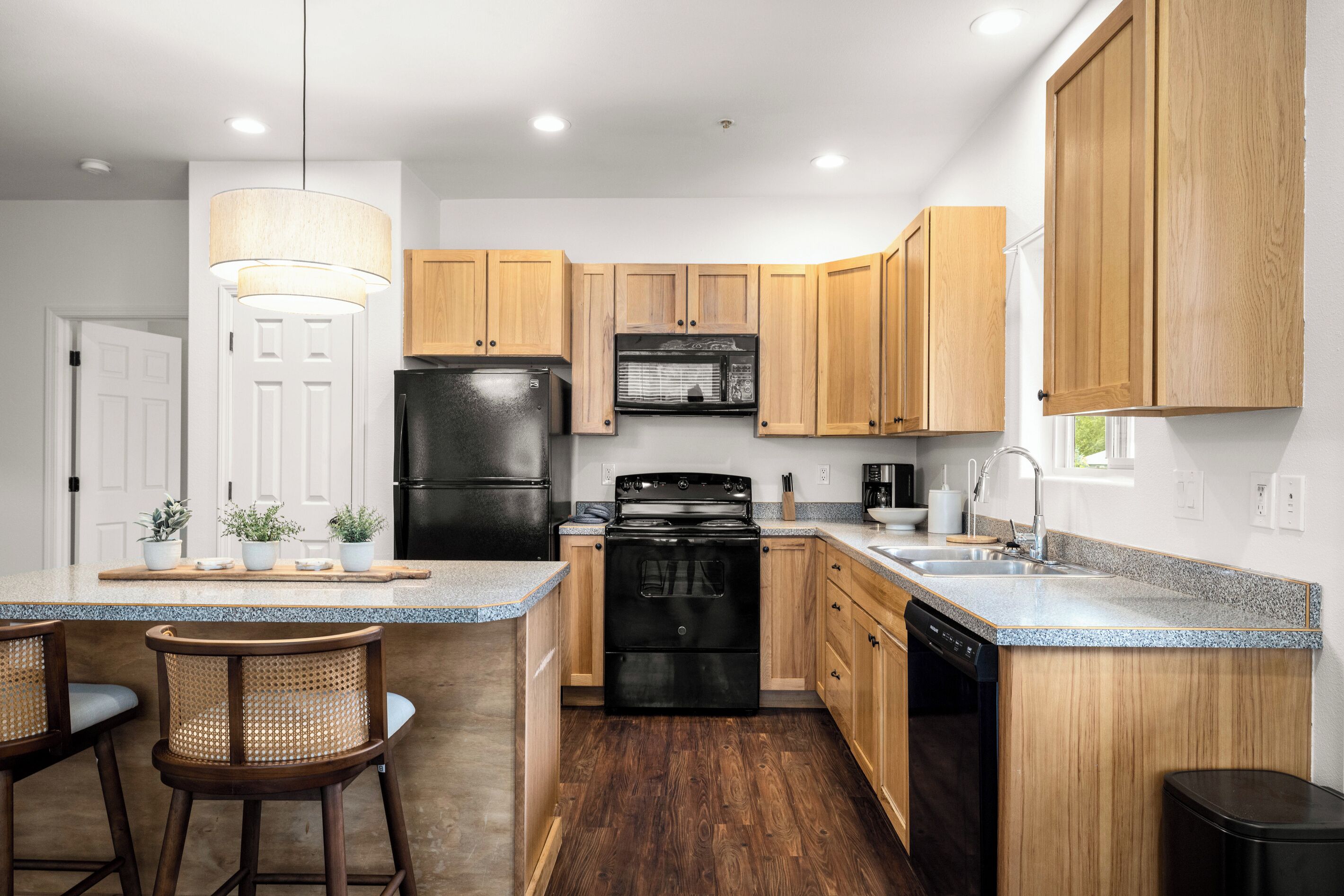 Une cuisine moderne avec des meubles en bois, un réfrigérateur noir, une cuisinière et un évier.
