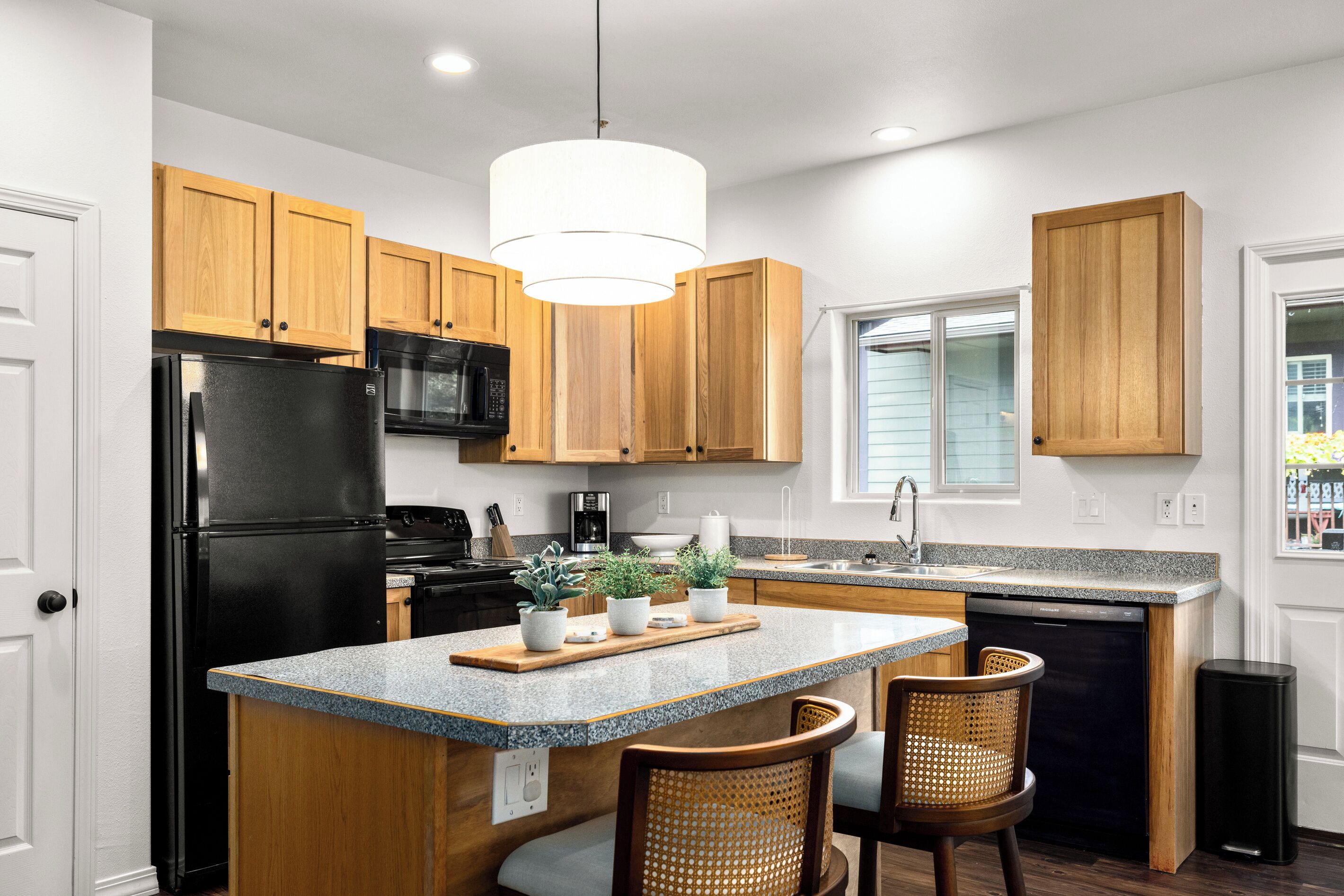 A kitchen with wooden cabinets, a black refrigerator, a microwave, a dishwasher, and a central island with chairs.