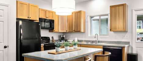 A kitchen with wooden cabinets, a black refrigerator, a microwave, a dishwasher, and a central island with chairs.