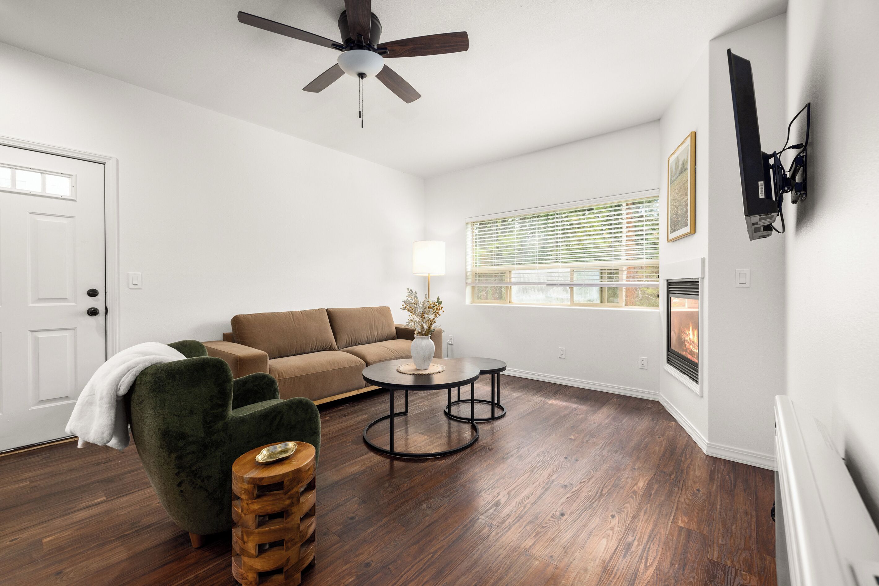 A living room with a brown sofa, a green armchair, a wooden coffee table, and a ceiling fan.