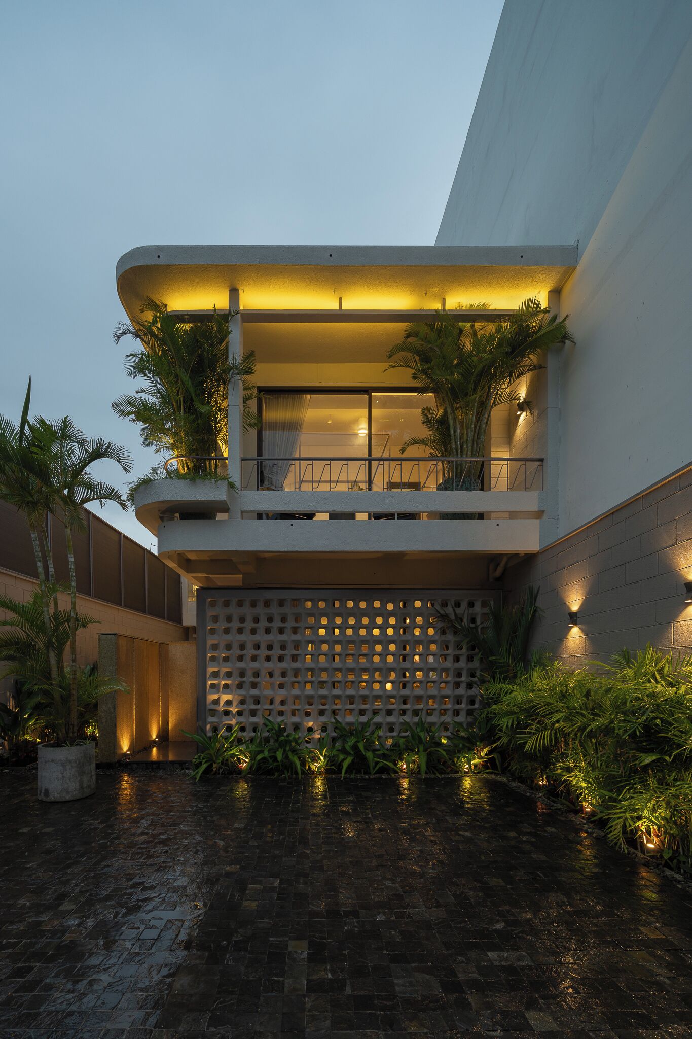 A modern building with a curved facade, a balcony with plants, and a water feature in the courtyard.
