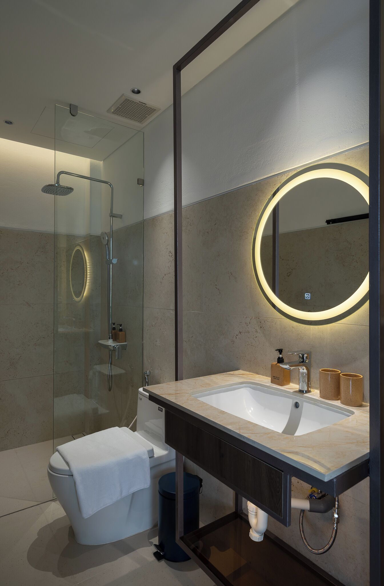 Een moderne badkamer met een douche met glazen wanden, een grote spiegel met ronde verlichting en een marmeren wastafel.