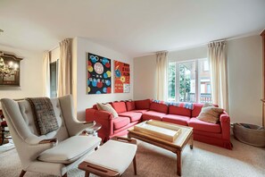 Ein Wohnzimmer mit einem roten Sofa, einem weißen Sessel, einem Holztisch und einer Pendelleuchte.