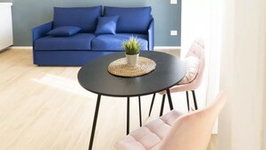 Ett rum med en blå soffa, ett runt svart bord med en vävd bordsduk och en rosa stol.