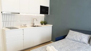 Ett modernt sovrum med en säng, ett sängbord och ett inbyggt köksutrymme med en diskho och en mikrovågsugn.