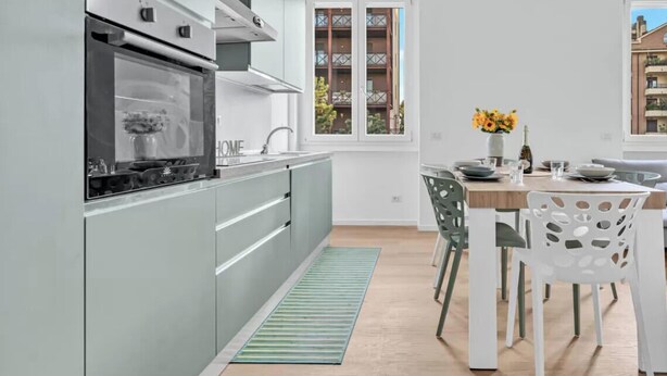 Et moderne køkken med indbygget ovn, et spiseområde med bord og stole, og et vindue med udsigt til bygninger.