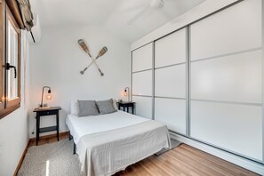 Quarto com cama, mesas de cabeceira, prateleira na parede e porta deslizante.