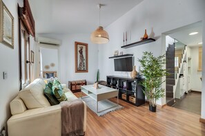 Uma sala de estar moderna com um sofá, mesa de centro e televisão. Uma escada leva a outro andar.