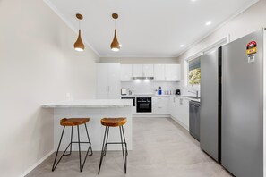 A modern kitchen with white cabinets, a central island with stools, a built-in oven, and a refrigerator with an energy rating sticker.