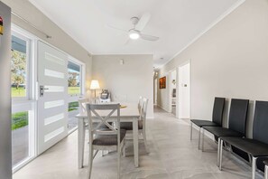 A spacious living area with a dining table, chairs, a sofa, and a ceiling fan.