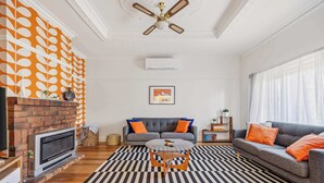 A living room with a fireplace, a sofa, a coffee table, and a patterned rug. - Brighton Belle — Mid-Century 2BR Home, Split Bath, Walk to Station & Main St (Stawell)