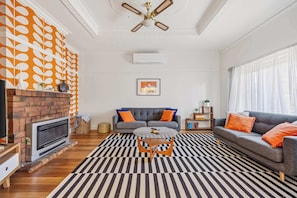 A living room with a fireplace, a sofa, a coffee table, and a patterned rug. - Brighton Belle — Mid-Century 2BR Home, Split Bath, Walk to Station & Main St (Stawell)