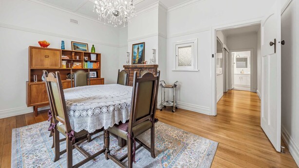 A dining room with a chandelier, wooden chairs, a lace tablecloth, a patterned rug, and a bookshelf with various items. - Brighton Belle — Mid-Century 2BR Home, Split Bath, Walk to Station & Main St (Stawell)