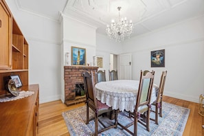 A dining room with a round table, wooden chairs, a chandelier, a fireplace, and artwork on the walls. - Brighton Belle — Mid-Century 2BR Home, Split Bath, Walk to Station & Main St (Stawell)
