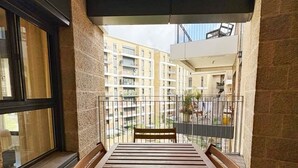 Un balcón con banca de madera, vista a un edificio de varios pisos y barandilla de metal.