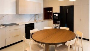 Una cocina moderna con una mesa redonda de madera, sillas blancas e iluminación colgante.
