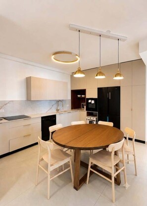 A modern kitchen with a round wooden table, white chairs, and pendant lighting. - Jerusalem Central - Spacious 3 Bedroom (Jerusalem)
