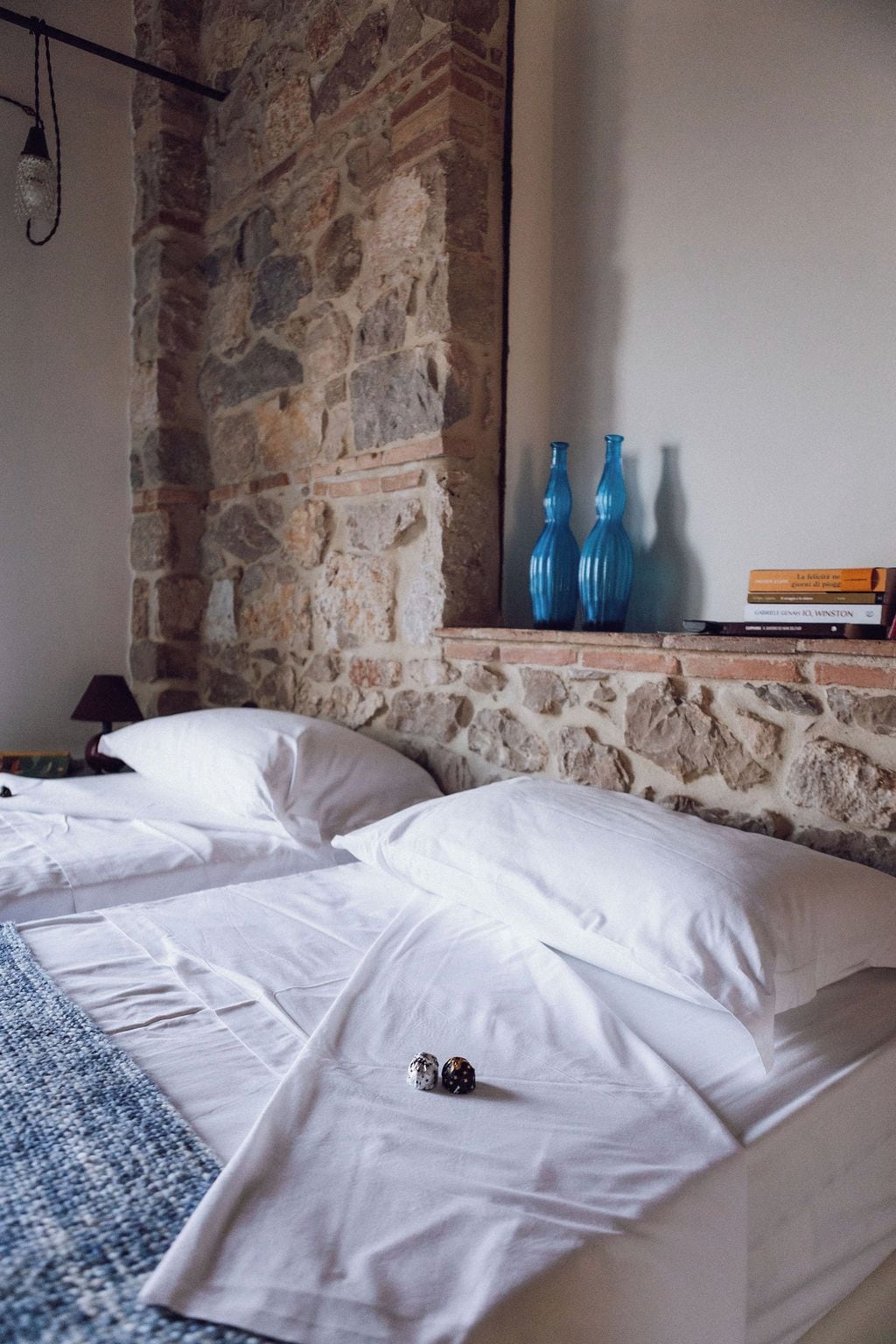Una stanza con due letti, un muro in pietra e una mensola con libri e vasi blu.