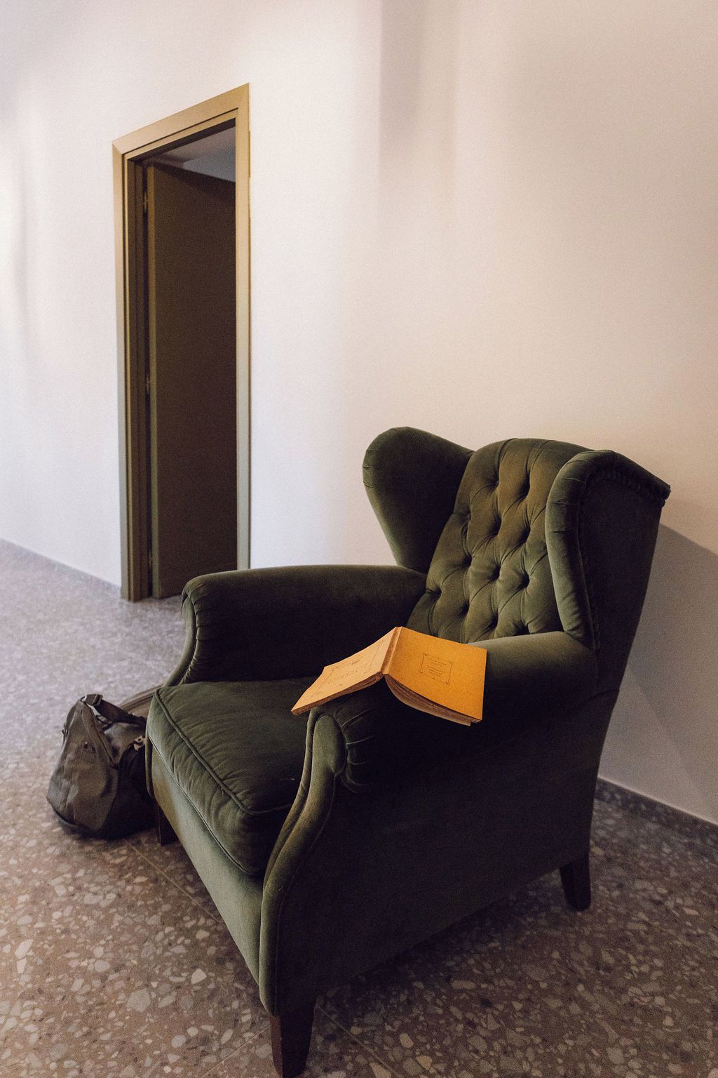 A dark green armchair with a book on it, a brown bag on the floor, and a door in the background.