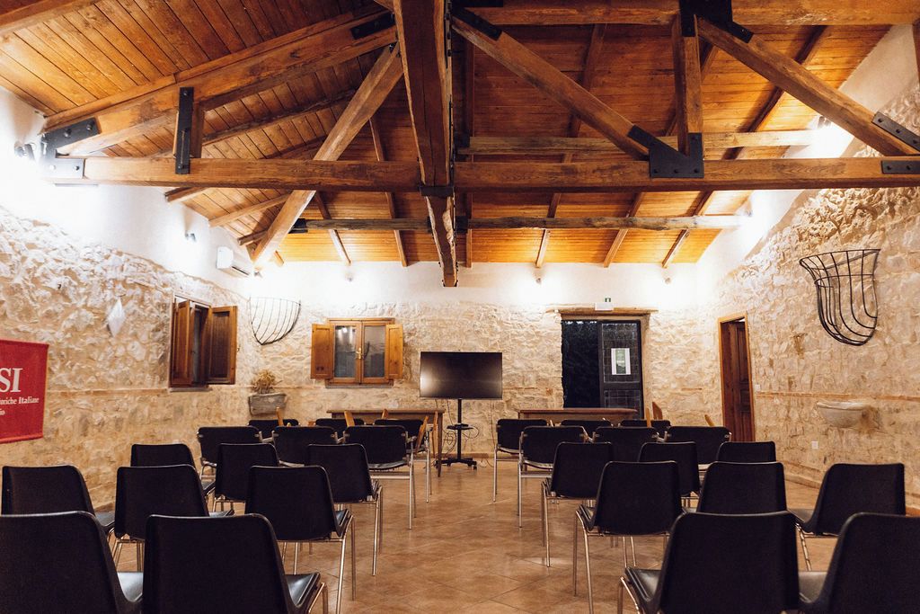 Un salón de conferencias con filas de sillas, un televisor y paredes de piedra.