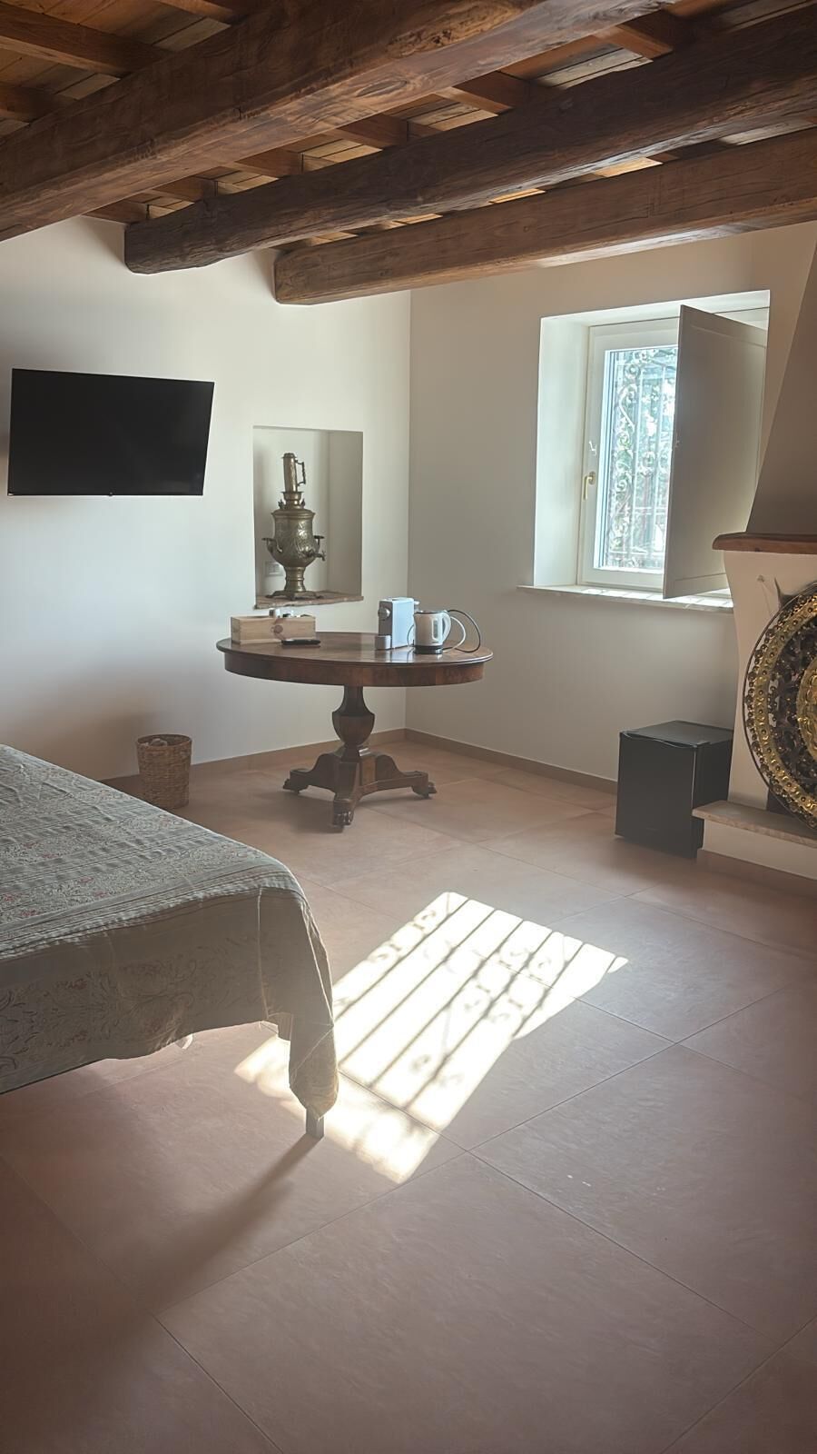 Una stanza con un letto, un tavolo rotondo con una lampada, una finestra e una TV fissata al muro.