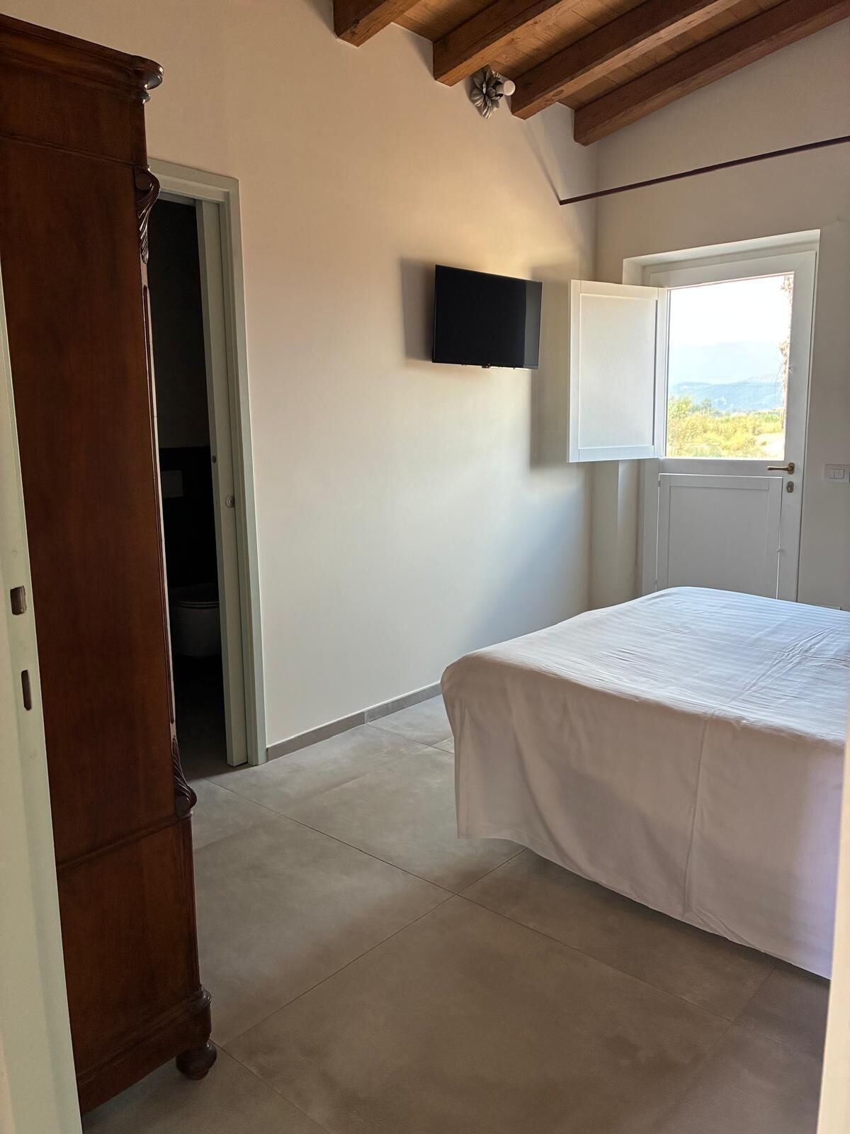 Ein Schlafzimmer mit einem Bett, einem an der Wand montierten Fernseher und einer Tür zu einem Balkon mit Blick.