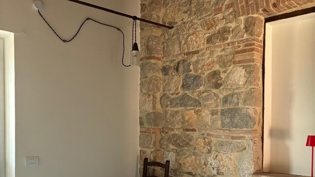 Un dormitorio con pared de piedra, una cama con ropa de cama a rayas, una silla de madera y una lámpara roja.