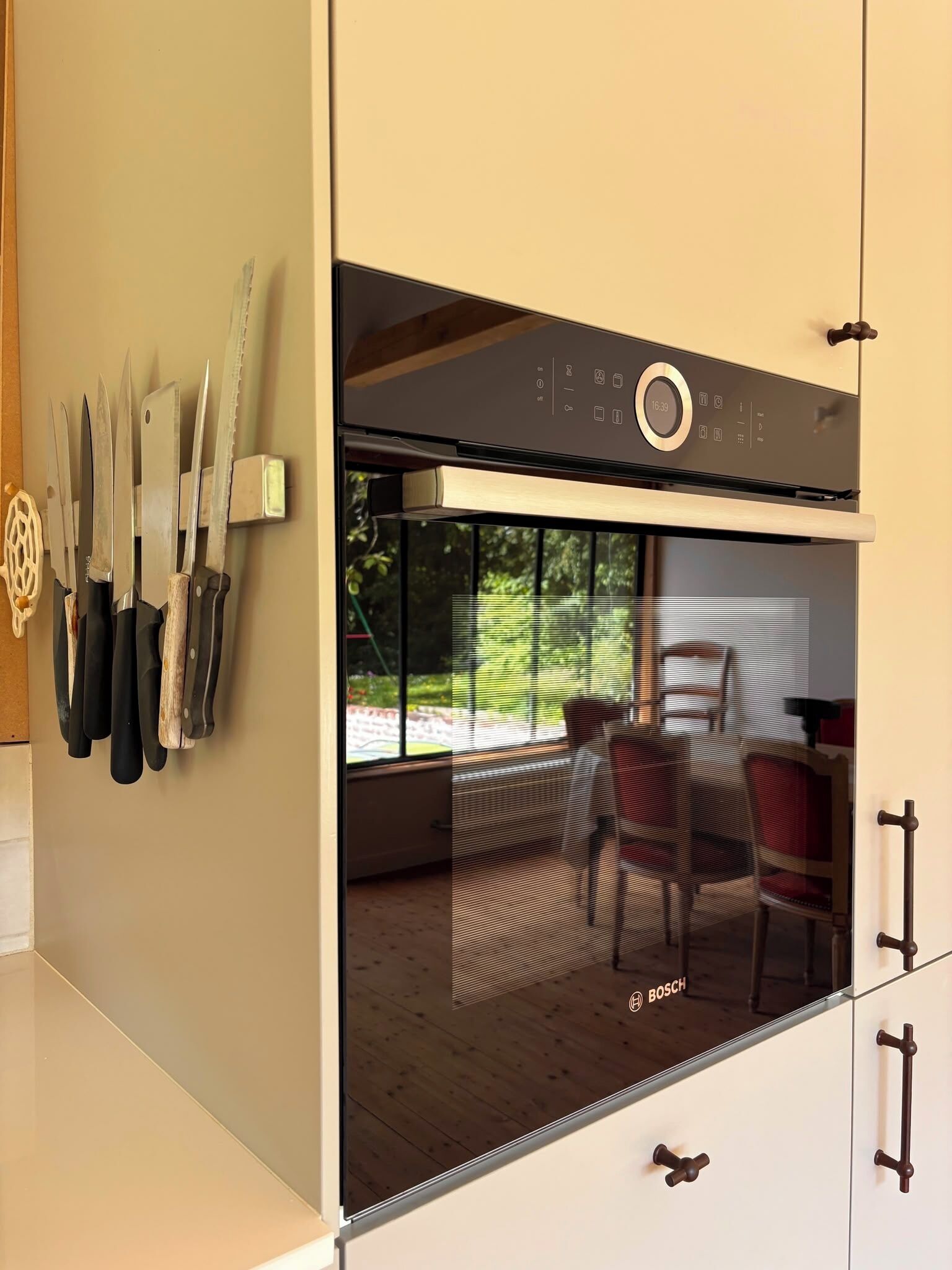 A kitchen with a Bosch oven, a window with a view of the outdoors, and knives hanging on the wall.