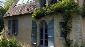 Ein rustikales Haus mit einem geneigten Dach, einem Schornstein und einem kleinen Garten mit Stufen zum Eingang.