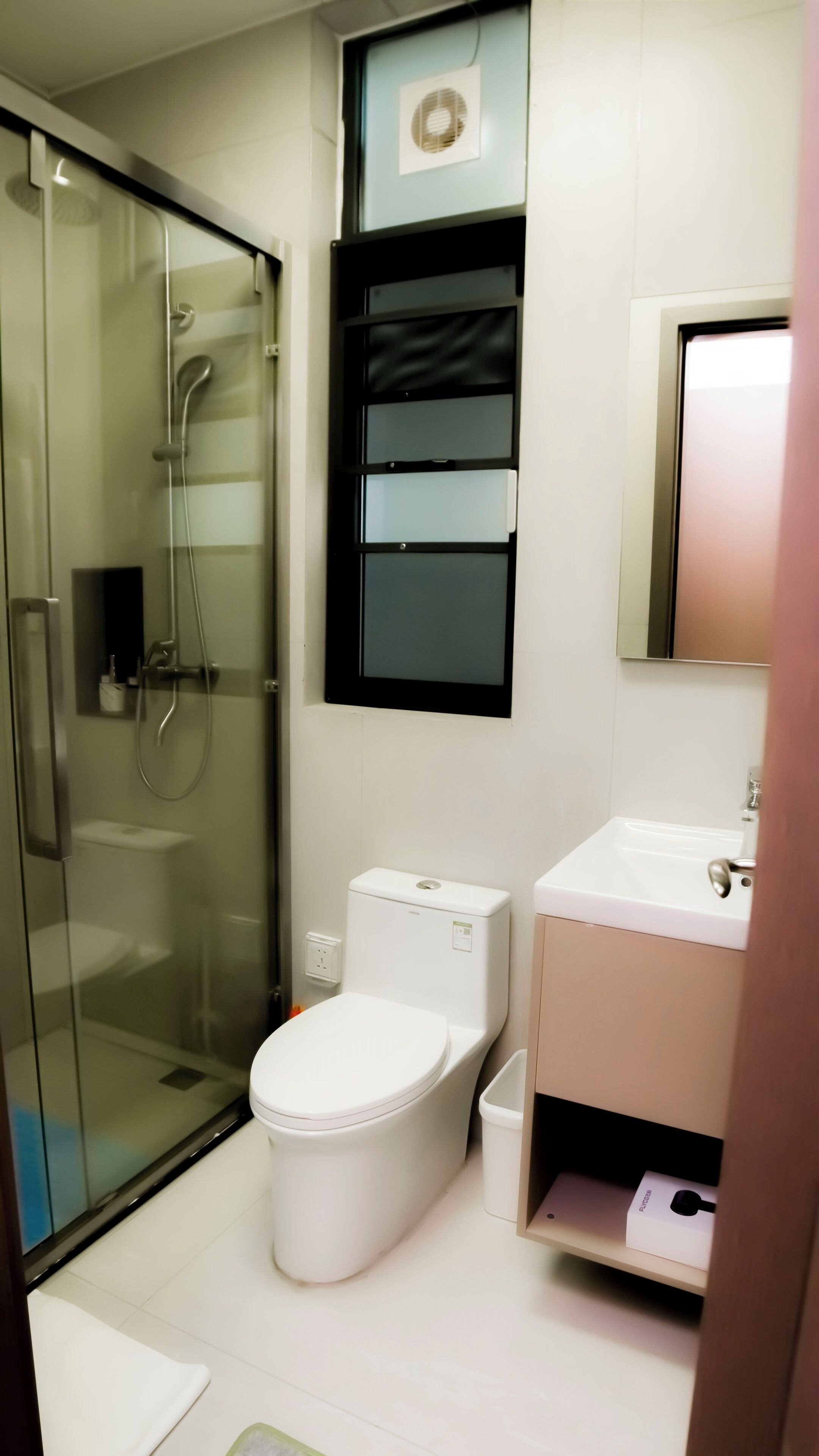 Un baño moderno con ducha envuelta en vidrio, inodoro blanco y lavamanos con espejo superior.