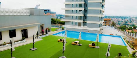 A rooftop pool with a view of the cityscape, surrounded by greenery and modern buildings.