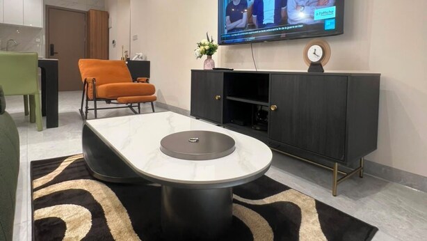 A modern living room with a flat-screen TV mounted on the wall, a round coffee table, a sofa, and a dining area in the background.