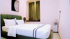 Una habitación de hotel con cama, lámpara, ventana con cortinas y aire acondicionado instalado en la pared.