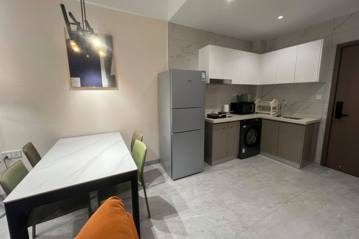 A modern kitchen with a dining area, including a refrigerator, microwave, sink, and washing machine.