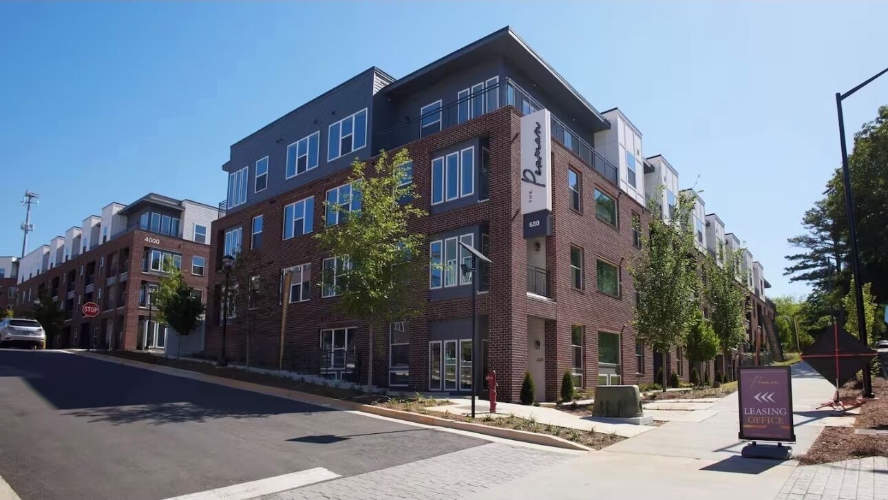 A multi-story building with a modern architectural design, featuring a mix of brick and glass facades, and a visible entrance with a signboard.