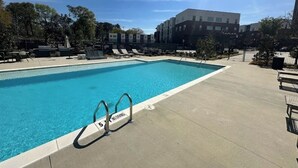 Una piscina con un letrero que prohíbe los clavados, rodeada de sillas de descanso y un edificio al fondo.